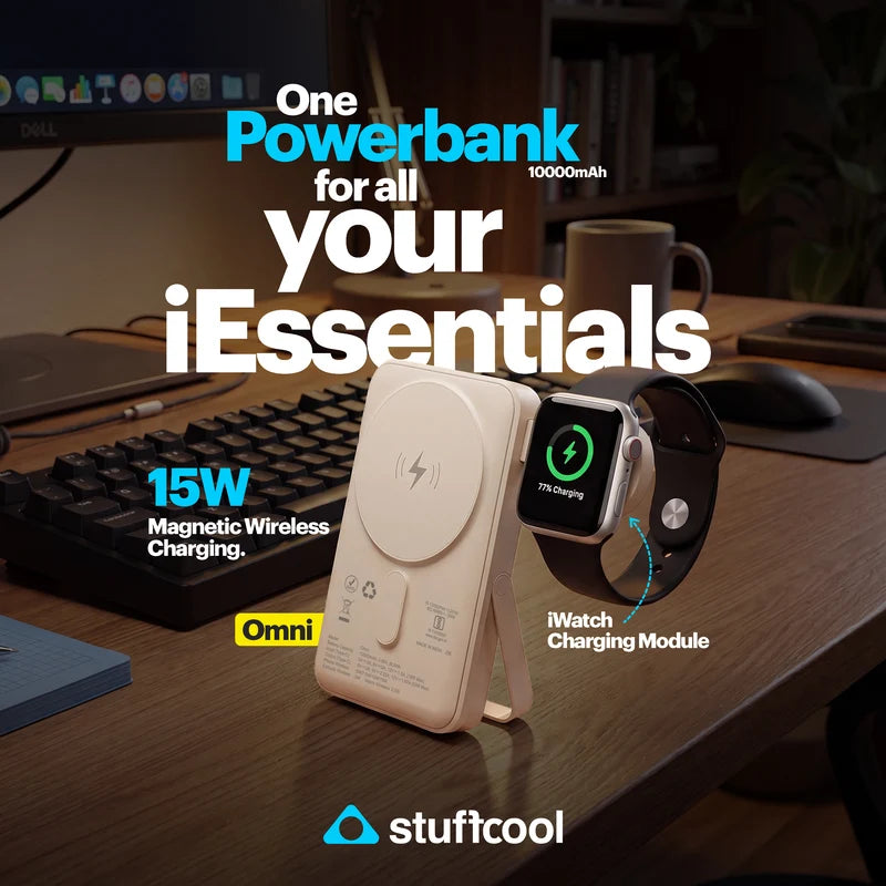 A white Omni wireless charging stand holding a white MagSafe-style charging case, with an Apple Watch shown beside it displaying 75% charging. The scene is set on a wooden desk with a keyboard, monitor, and mug in the background, with large promotional text reading 'One Powerbank for all your iEssentials' and the Stuffcool logo at the bottom.