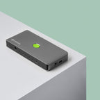 A gray rectangular electronic device with a green circular button, branded 'CLOVER', resting on a white platform against a light green background.