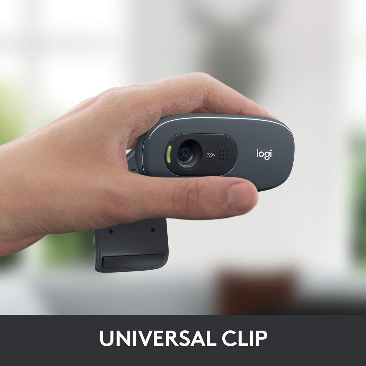 Logitech webcam with a universal clip held by a hand against a blurred background