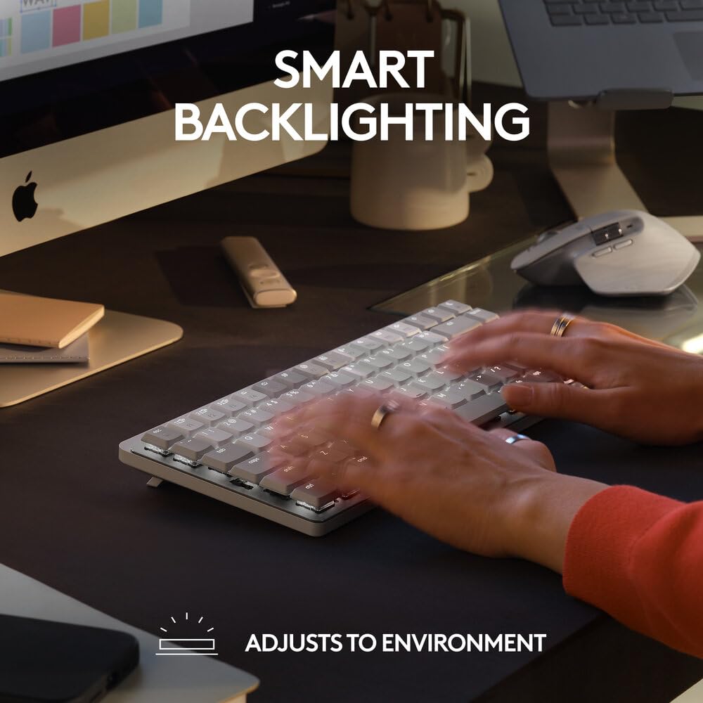 A close-up of a person typing on a slim white and silver keyboard on a dark desk, with large text reading 'SMART BACKLIGHTING' and smaller text 'ADJUSTS TO ENVIRONMENT' overlaid on the scene.