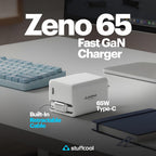 A white Stuffcool Zeno 65 Fast GaN Charger with a built-in retractable cable, shown on a desk next to a keyboard, laptop, and notebook. The image features promotional text overlays.