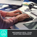 Person typing on a mechanical keyboard with a desk setup including a laptop, headphones, and stationery.