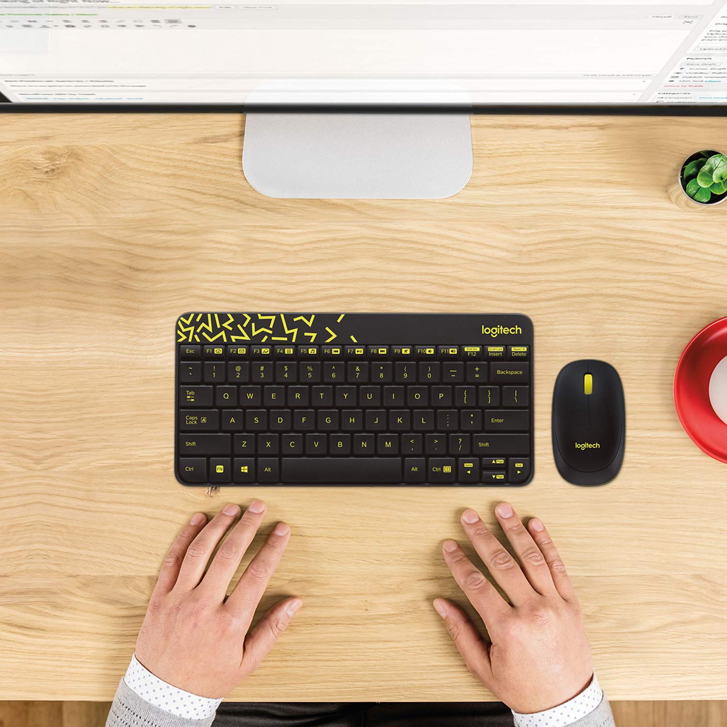 Logitech keyboard and mouse set on a wooden desk with a computer monitor in the background.