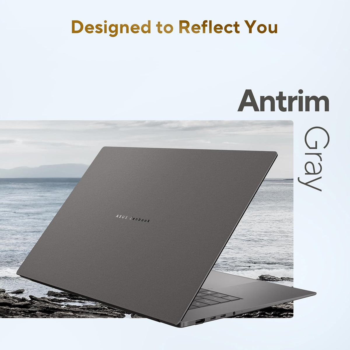 A dark gray laptop shown open at an angle over a coastal scene, with text reading 'Designed to Reflect You' and 'Antrim Gray' on a pale background.