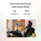 Promotional graphic with the headline 'Tune into the future, hear every detail' and feature icons for webcam privacy and Dolby Atmos. Below, a person wearing over-ear headphones relaxes in a chair using a laptop in a modern room.