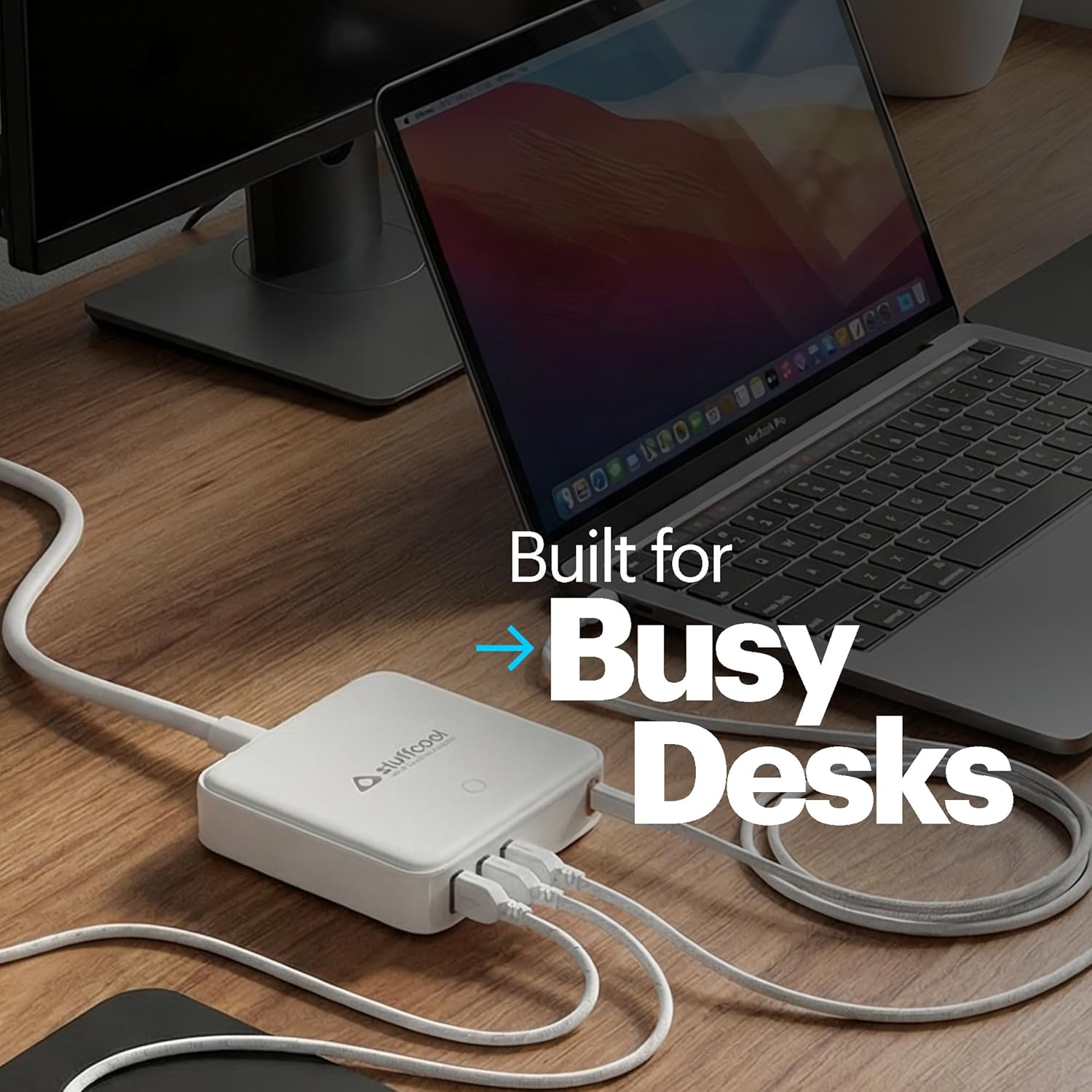 A white Bulldogs multi-port hub with attached white cables, shown on a wooden desk next to an open laptop and mouse. White text overlay reads 'Built for Busy Desks'.
