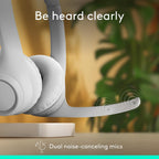 White headphones with dual noise-canceling mics on a blurred indoor background