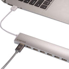 A silver CADYCS USB hub with multiple ports, shown connected to a white cable and plugged into a silver laptop on a white background.