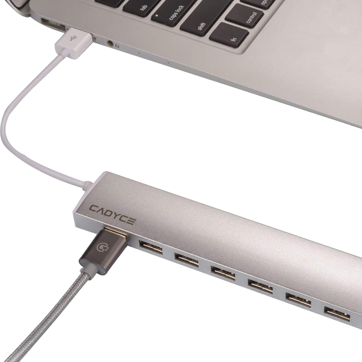 A silver CADYCS USB hub with multiple ports, shown connected to a white cable and plugged into a silver laptop on a white background.