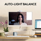 Computer monitor displaying a video call with auto-light balance feature, on a desk with a plant and mug.