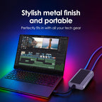 A silver portable power adapter with blue LED cable lighting shown next to an open laptop on a dark surface with colorful neon reflections. White text at the top reads 'Stylish metal finish and portable' and 'Perfectly fits in with all your tech gear'.