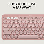 A close-up of a Logitech wireless keyboard in a dusty rose pink color, featuring a clean, minimalist layout with a white top bar and white printed key labels. Above the keyboard, bold black text reads 'SHORTCUTS JUST A TAP AWAY'.