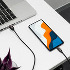 Smartphone with a colorful display connected to a laptop on a white surface.