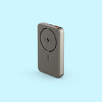 A slim, rectangular portable power bank in a metallic taupe-gray finish, featuring a black wireless charging symbol on its front face, set against a solid light blue background.