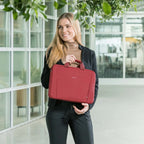 Woman holding a red bag in an indoor setting with large windows and plants.