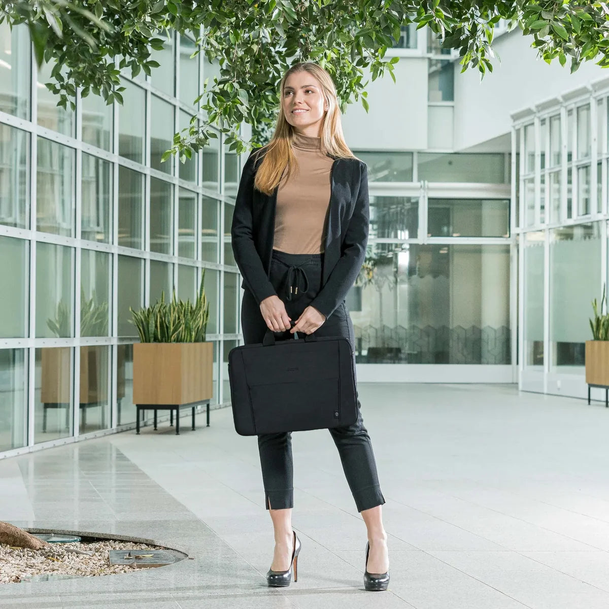 Woman holding a black briefcase in an office building courtyard