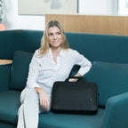 Woman sitting on a teal couch holding a black bag in an indoor setting.