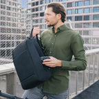 Man holding a black backpack against an urban background