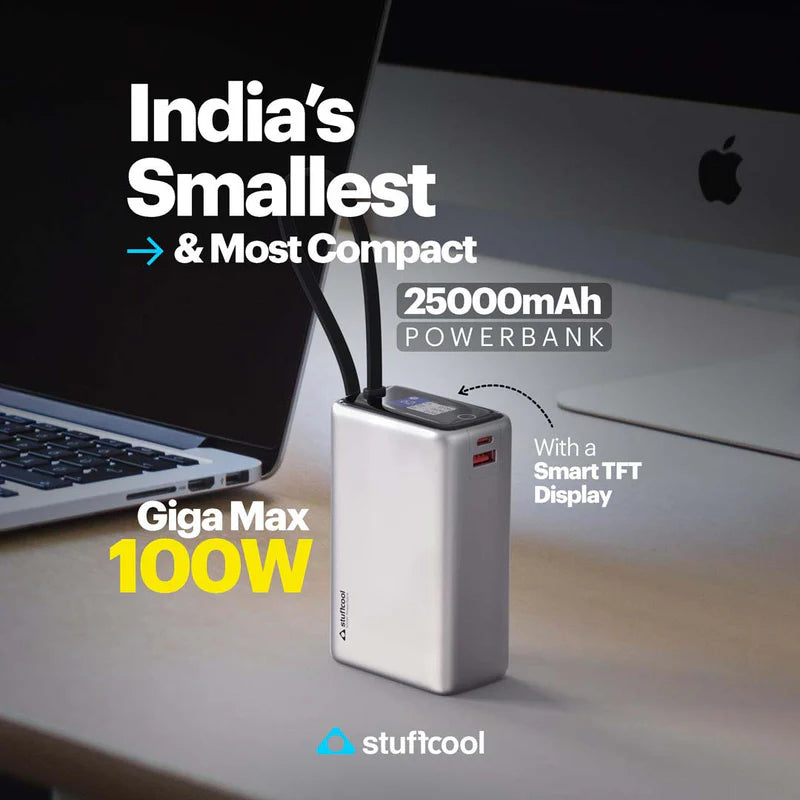 A silver power bank with a small display and two antennas, shown on a desk next to a laptop and computer monitor. Text overlays read 'India's Smallest & Most Compact', '25000mAh POWERBANK', 'Giga Max 100W', and 'With a Smart TFT Display'.