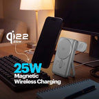 A silver magnetic wireless charging dock shown on a desk beside a black smartphone, with overlaid text reading 'qi22 25W Magnetic Wireless Charging' and '25W Magnetic Wireless Charging.' The scene includes a keyboard, lamp, monitor, and notebook in a real indoor environment, so this is Lifestyle rather than Product/Packaging.