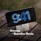 A smartphone resting on a white stand on a wooden table outdoors, with a large blue digital clock display on the phone screen and overlaid text reading 'Access Standby Mode'.