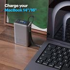 A portable power bank with a black cable connected to a laptop on a wooden desk, with a framed print in the background and text reading 'Charge your MacBook 14"/16"'.