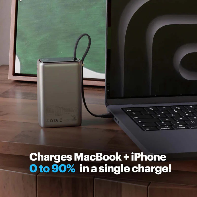 Portable power bank charging a MacBook and iPhone on a wooden desk.